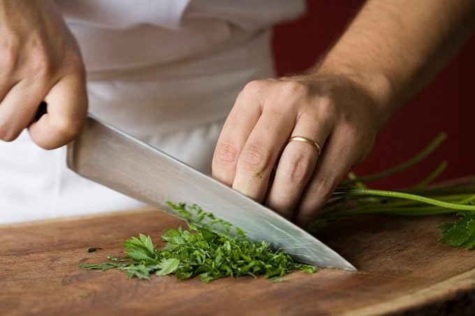 Person chopping parsley with a chef's knife on a wooden cutting board