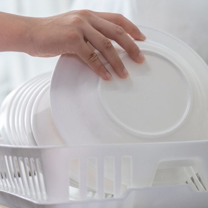 Hand of woman putting just washed clean plate in the dish rack